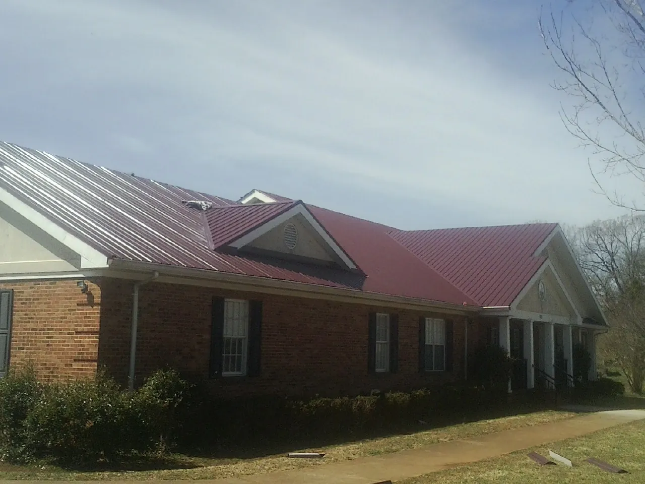Red metal roof with gabled entries on a long brick building, from a Hail Damage Roof Repair job in Crawfordville