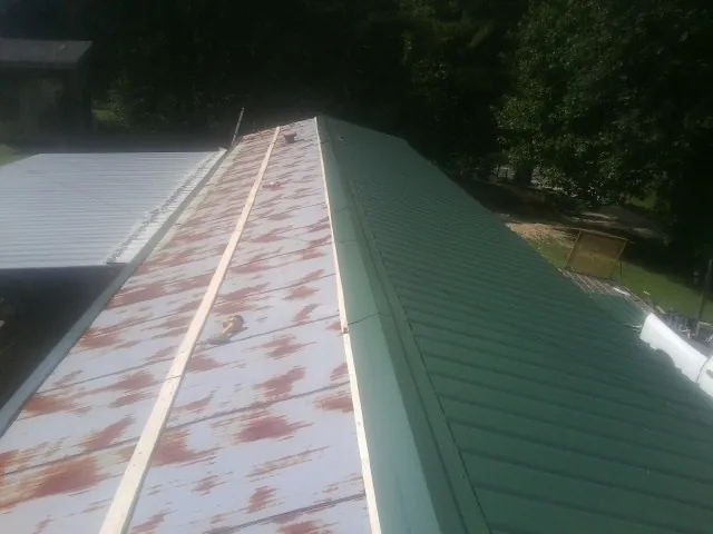 Old rusted panels beside newly installed green metal roofing — Wind Damage Roof Repair by Roofing Brothers in Crawfordville