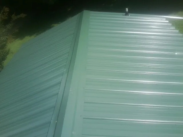 New green metal panels meeting at the ridge of a roof — Flat Roof Repair work by our crew in Crawfordville