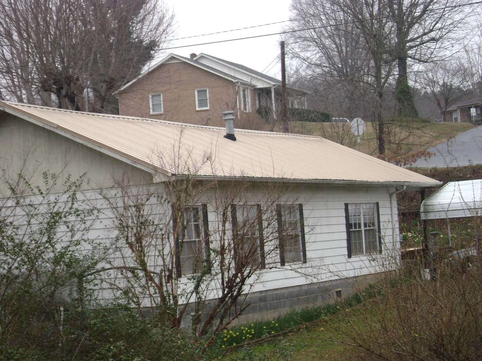 Tan metal roof on a white sided house set into a hillside — Commercial Roofing by Roofing Brothers in Crawfordville
